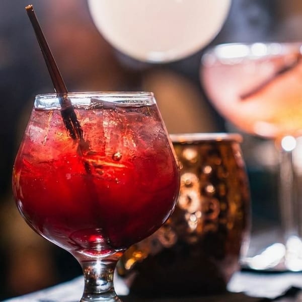 Three cocktails on a bar, a red drink with a straw in the foreground.