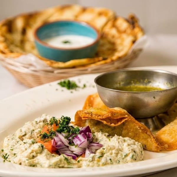 A plate of fried dumplings, a creamy dip with red onions, and a basket of flatbread with a dip.