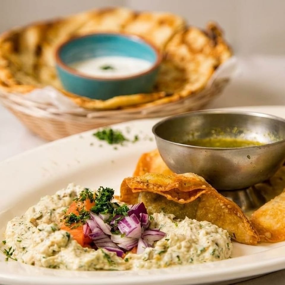 A plate of fried dumplings, a creamy dip with red onions, and a basket of flatbread with a dip.