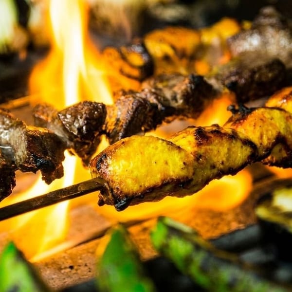 Skewers of chicken and beef kebabs grilling over open flames with vegetables.