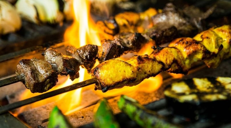 Skewers of chicken and beef kebabs grilling over open flames with vegetables.