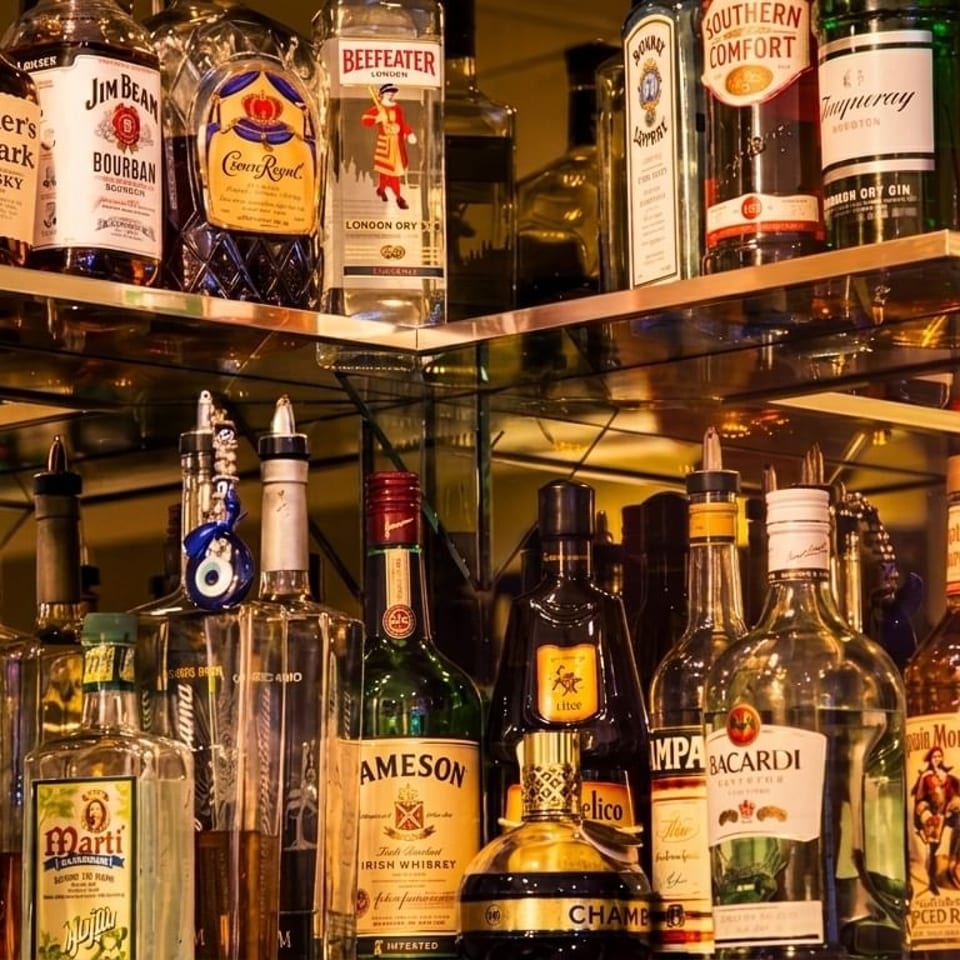 A well-stocked bar shelf with various liquor bottles, including whiskey, rum, gin, and vodka.