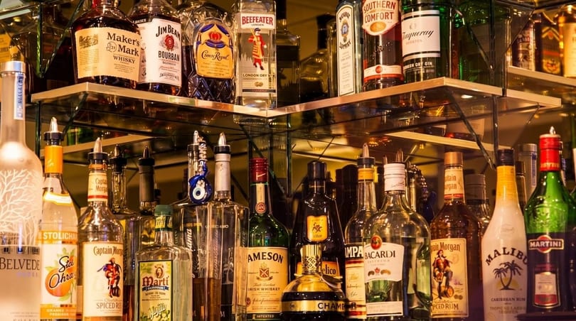 A well-stocked bar shelf with various liquor bottles, including whiskey, rum, gin, and vodka.