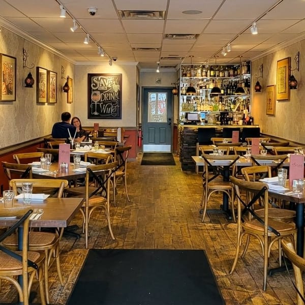 A restaurant dining room with wooden tables and chairs, a bar, and decorative mirrors.
