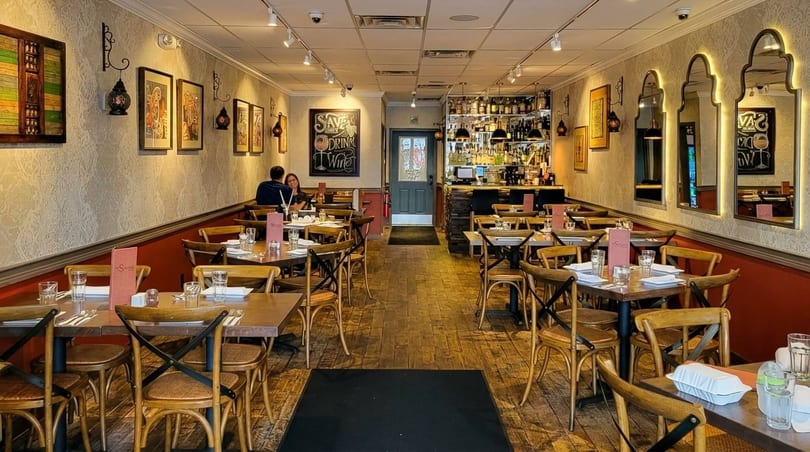 A restaurant dining room with wooden tables and chairs, a bar, and decorative mirrors.