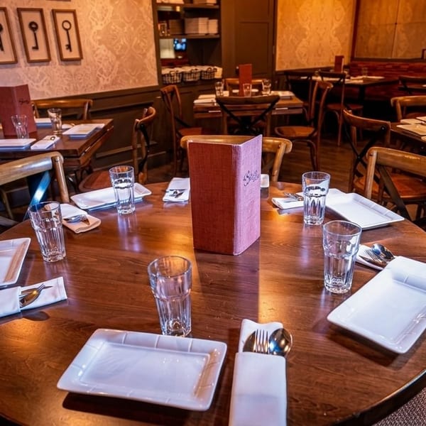 Cozy restaurant interior with round wooden tables set with white plates, glasses, and menus.