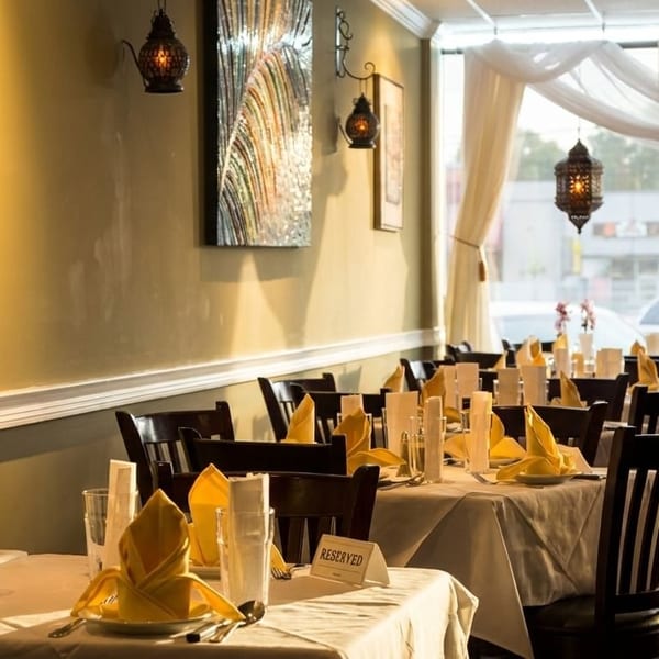 Restaurant interior with set tables, yellow napkins, dark chairs, and decorative wall art and lanterns.