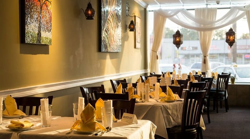 Restaurant interior with set tables, yellow napkins, dark chairs, and decorative wall art and lanterns.