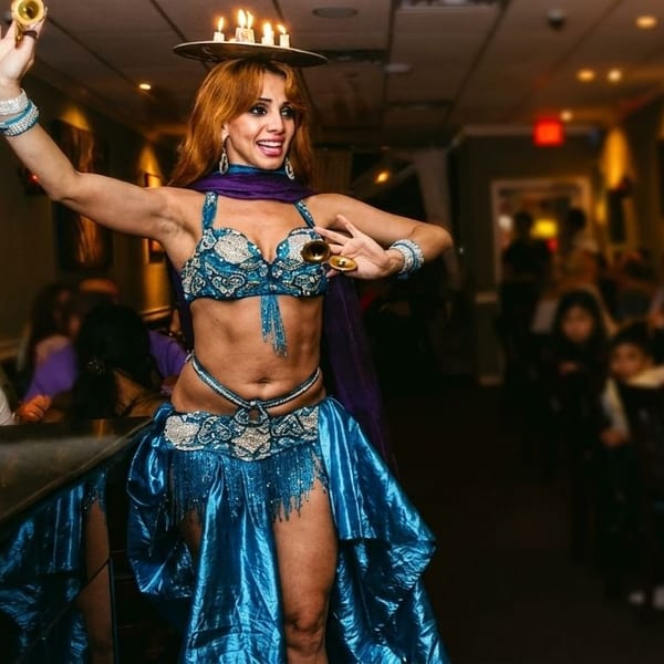A belly dancer in a blue costume with candles on her head performs for restaurant patrons.