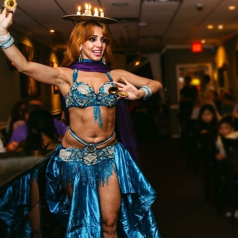 A belly dancer in a blue costume with candles on her head performs for restaurant patrons.